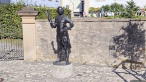 Lebensgroße Balthasar-Neumann-Statue im Schatten der von ihm erbauten Kreuzkapelle.